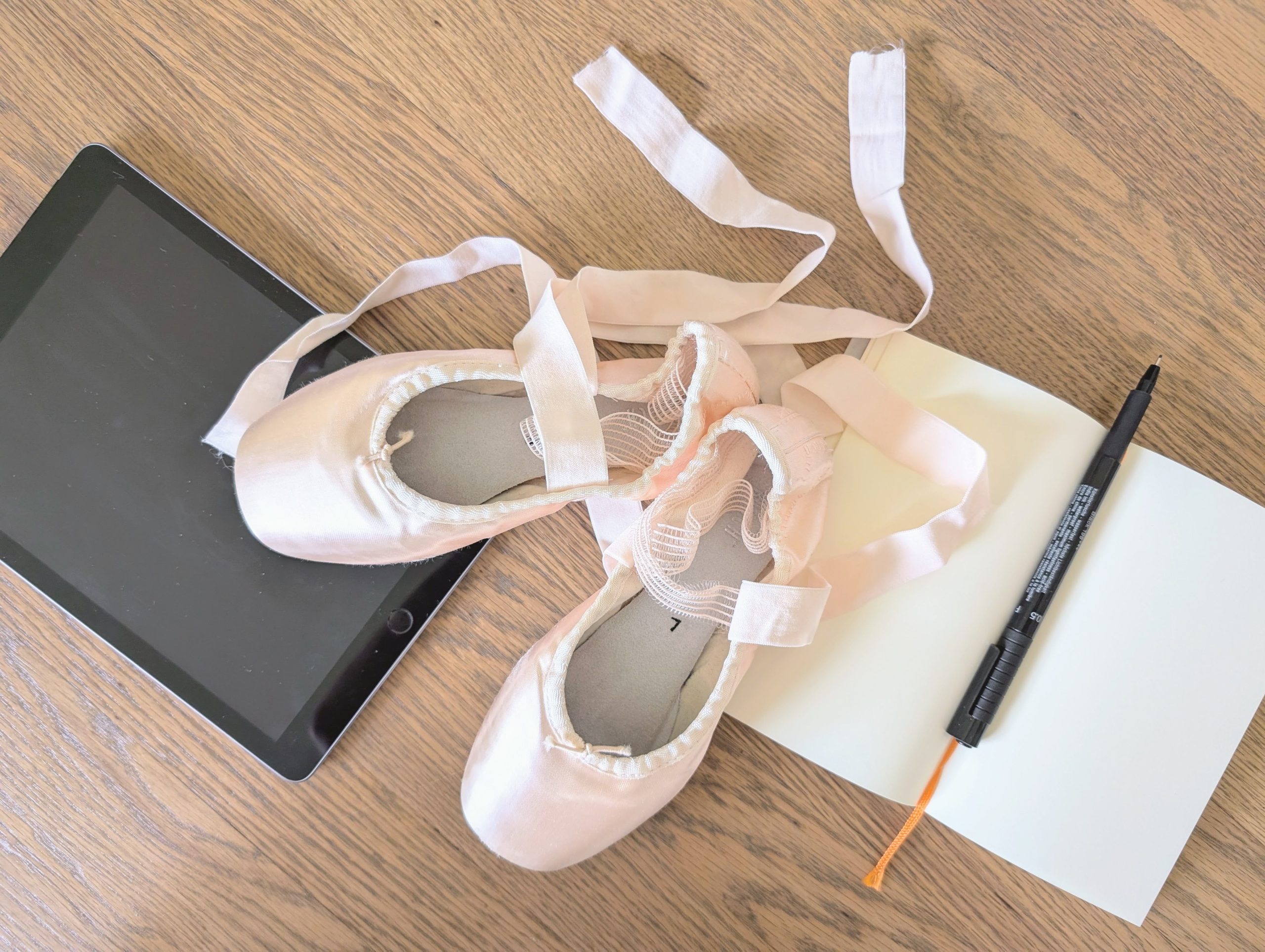 Pointe shoes with a notebook, pen, and tablet